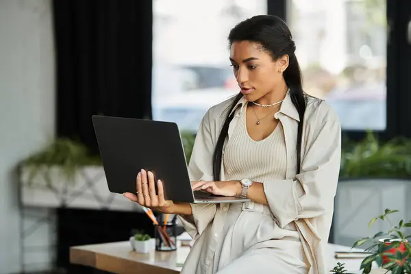 A young woman attentively uses her laptop in a modern, plant filled office. — Stock Photo