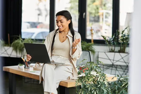 In a chic office setting, a young woman smiles and gestures during a video call on her laptop. — Stock Photo
