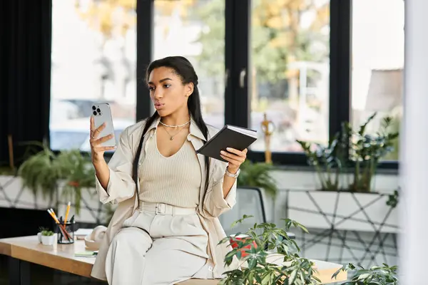 Una giovane donna bilancia la sua attenzione tra il suo smartphone e un notebook mentre lavora. — Foto stock