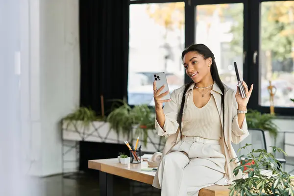 Uma jovem mulher confiantemente se envolve com seu smartphone e notebook, mostrando sua criatividade. — Fotografia de Stock