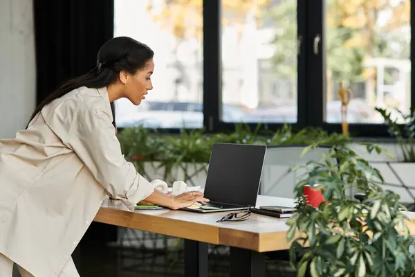 In a bright office setting, a young woman leans over her laptop, deeply focused and engaged. — Stock Photo