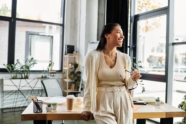 A beautiful young woman stands thoughtfully in her modern office, gazing out the window. — Stock Photo