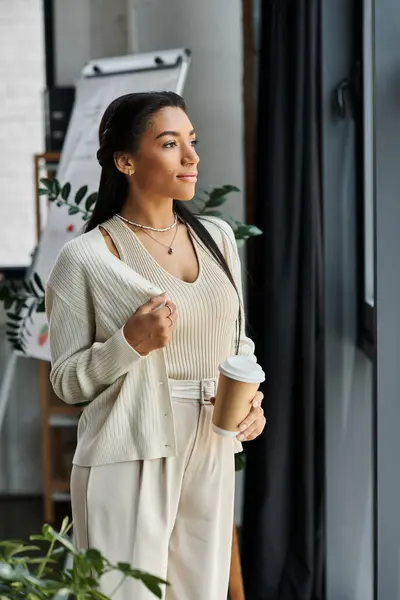A young woman in smart attire takes a moment to reflect, holding a cup of coffee in her office. — Stock Photo