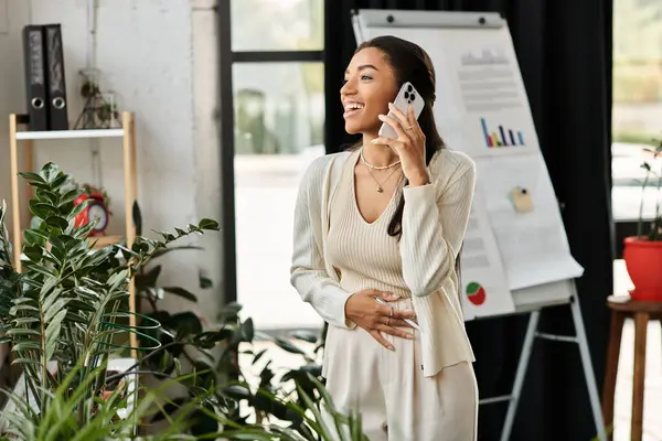 A young woman is happily talking on her phone, surrounded by plants and office decor. — Stock Photo