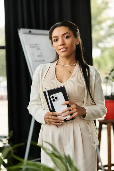 Una giovane donna si trova fiduciosa in un ufficio, con un quaderno in mano e immersa nel verde. — Foto stock