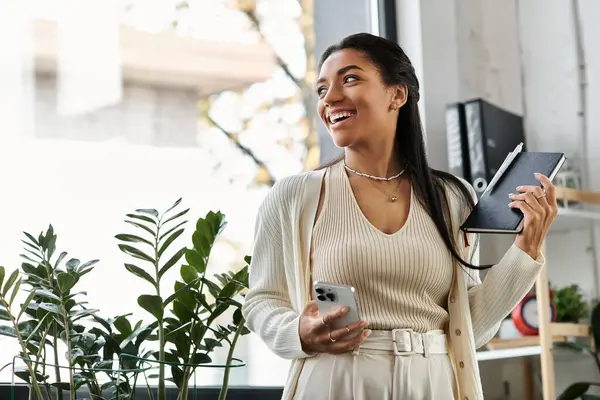 Eine junge Frau organisiert freudig ihre Arbeit, während sie das Tageslicht in ihrem Büro genießt. — Stockfoto