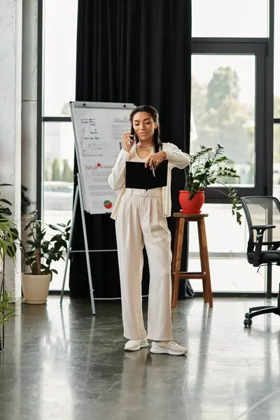 A young woman engages on a phone call while standing in a chic office space with greenery. — Stock Photo