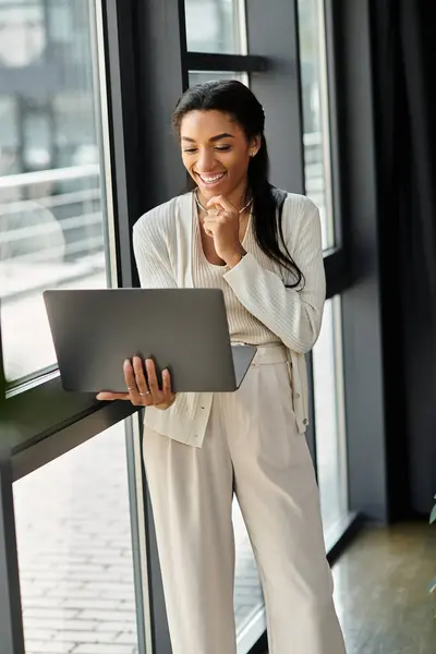A smiling woman in office attire enjoys her work at a laptop, surrounded by natural light. — Stock Photo