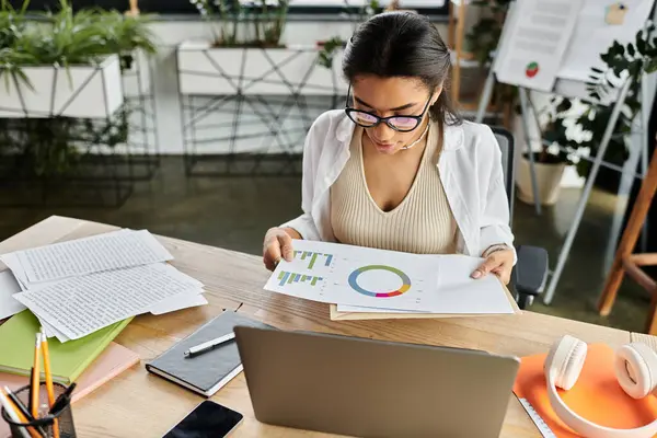Uma jovem se concentra em analisar gráficos coloridos enquanto está sentada em sua mesa de escritório organizada. — Fotografia de Stock