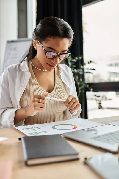 A focused young woman reviews colorful graphs and charts in a busy workspace. — Stock Photo