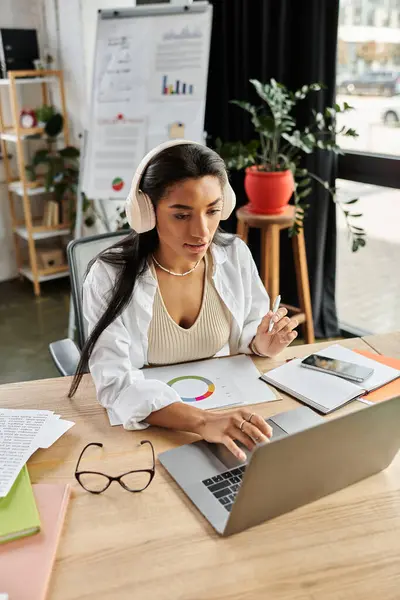 A young woman engages in work at her desk, analyzing data and wearing headphones. — Stock Photo
