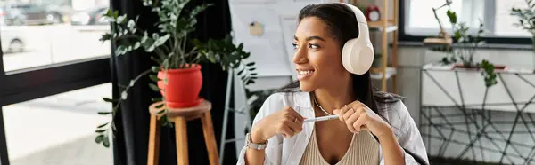 Una joven sonríe mientras trabaja en su escritorio, inmersa en sus tareas con auriculares puestos. - foto de stock