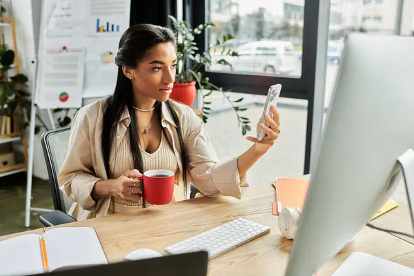 In a modern office, a young woman relaxes with a cup of coffee while using her smartphone. — Stock Photo