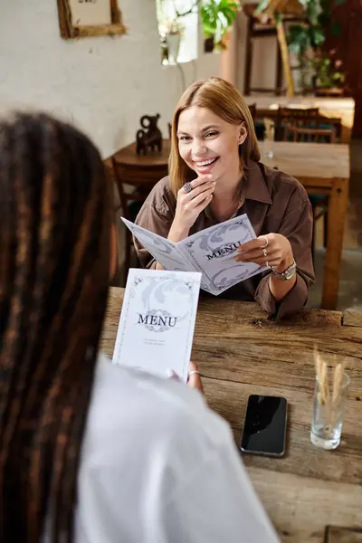 Dos mujeres, profundamente enamoradas, disfrutan de su cita en el café, compartiendo risas y opciones de menú sobre el café. - foto de stock