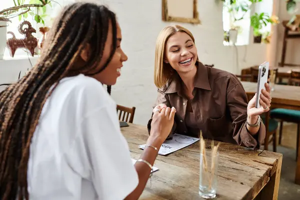 Eine Afroamerikanerin mit Zöpfen lächelt ihre Freundin freundlich an, während sie ihr Café-Date genießt. — Stockfoto