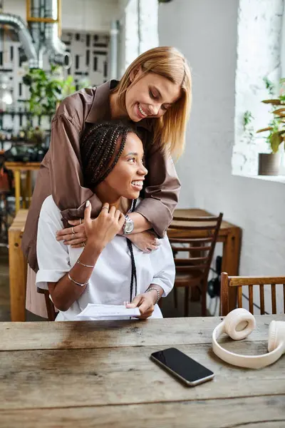 A smiling African American woman receives a sweet embrace from her girlfriend at a cozy cafe. — Stock Photo