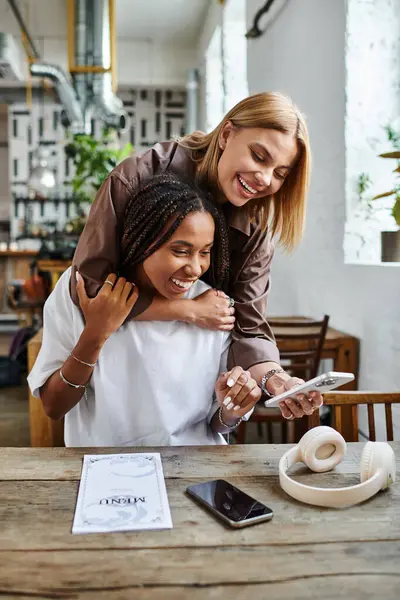 Dos mujeres comparten la risa y la alegría en un café, disfrutando de la compañía de los demás con sonrisas y tecnología. - foto de stock