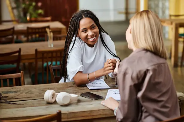 Dans un café animé, deux femmes se connectent intimement, partagent des sourires et embrassent un moment d'amour. — Photo de stock