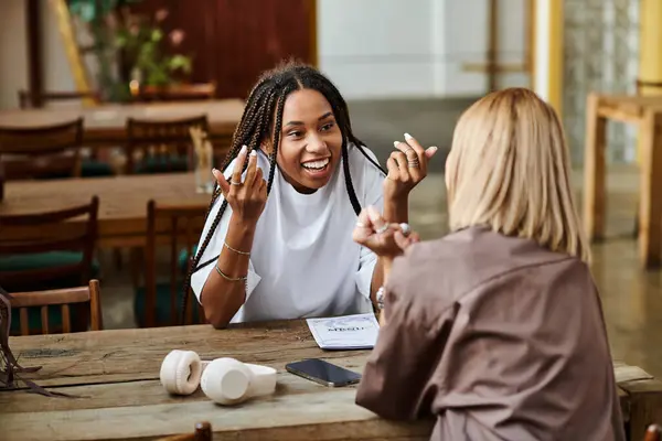 A happy African American woman shares laughter with her girlfriend at their favorite cafe. — Stock Photo