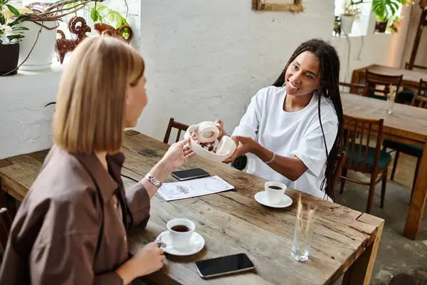A smiling African American woman with braids shares a moment with her girlfriend at a cafe. — Stock Photo