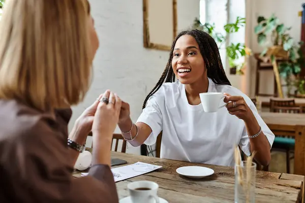 A smiling African American woman shares a warm moment with her girlfriend over coffee in a cozy cafe. — Stock Photo