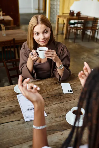 In a vibrant cafe, a multicultural lesbian couple shares heartfelt smiles while enjoying their coffee together. — Stock Photo