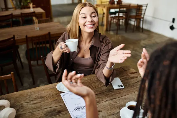 A cheerful African American woman shares a warm moment with her girlfriend over coffee at a cafe — Stock Photo