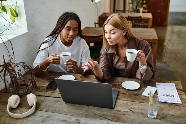 A smiling African American woman shares a light moment with her girlfriend over coffee at a cafe. — Stock Photo