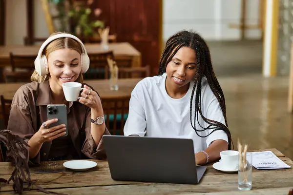 Two women share laughter and love over coffee, with one checking her phone and the other smiling brightly. — Stock Photo