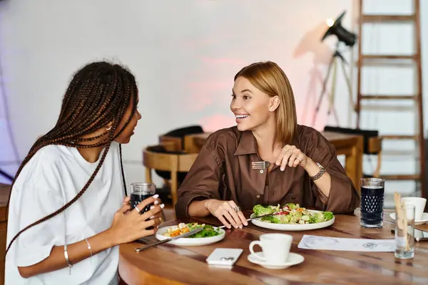 A joyful African American woman shares a playful moment with her girlfriend over brunch at a cafe. — Stock Photo