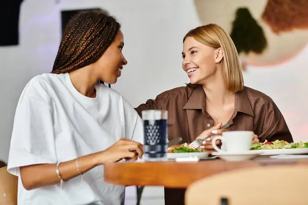 Two women share a joyful moment at a cafe, smiles and affection illuminating their lunchtime together. — Stock Photo