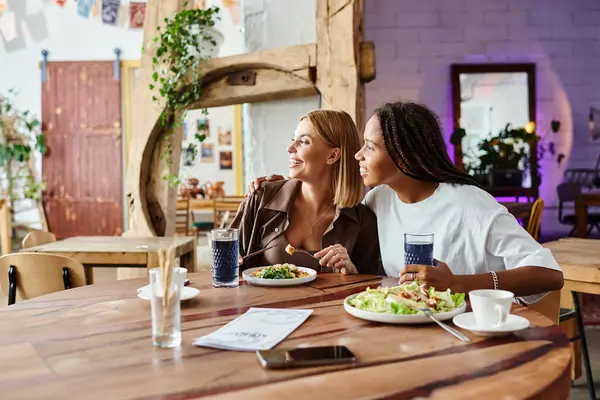 A happy multicultural couple sits at a cozy cafe, enjoying delicious food and smiles in each others company. — Stock Photo
