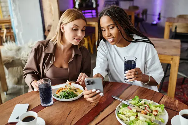 A smiling couple enjoys a meal at a charming cafe, capturing a special moment on their phone. — Stock Photo