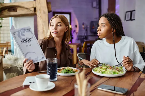 An African American woman with braids and her girlfriend share a warm moment in a cafe while looking at the menu. — Stock Photo