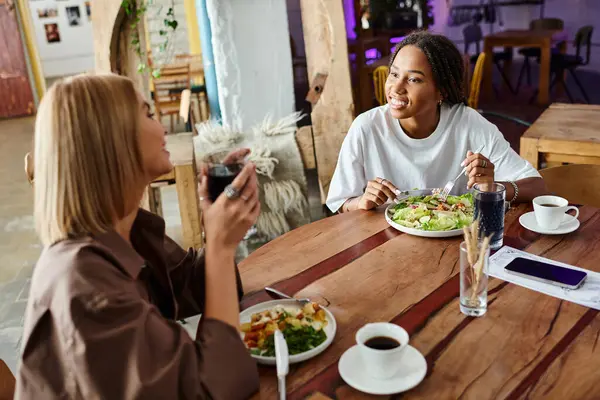 Dans un charmant café, une femme afro-américaine souriante partage un délicieux repas avec sa petite amie. — Photo de stock