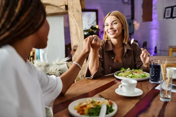 In a vibrant cafe, a joyful couple of different backgrounds shares a lovely lunch while smiling and engaging. — Stock Photo