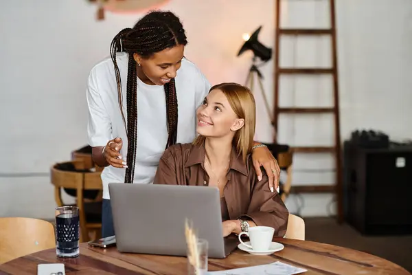 A smiling African American woman shares a warm moment with her girlfriend at a cafe while they work. — Stock Photo