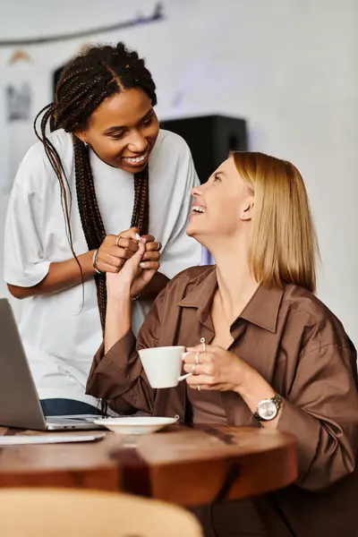 An African American woman with braids shares a joyful moment with her girlfriend over coffee in a cafe. — Stock Photo