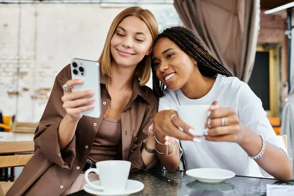 In einem warmen Café lacht ein Pärchen, während eine mit einer Tasse Kaffee auf ihr Handy schaut.. — Stockfoto