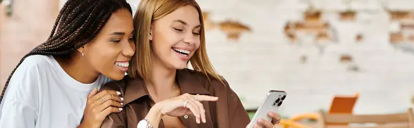 Two women delight in each others company, laughing as they share something on a phone at a cafe — Stock Photo