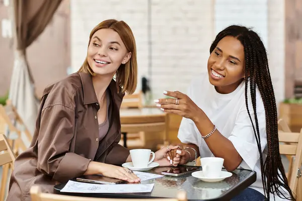 A happy lesbian couple chats and laughs while sharing coffee in a lively cafe setting. — Stock Photo