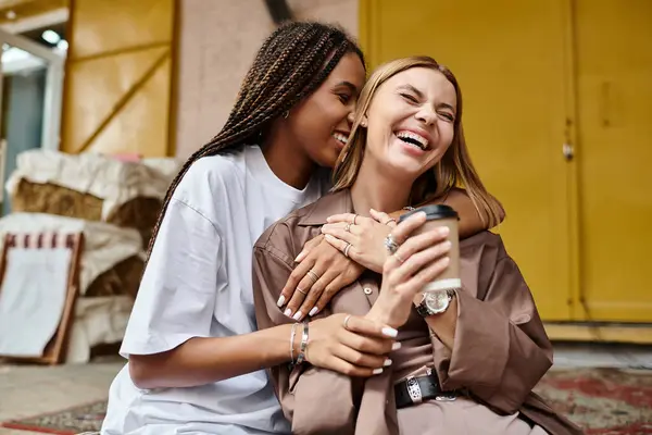 A cheerful African American woman embraces her girlfriend at a cafe, both enjoying a joyful moment together. — Stock Photo