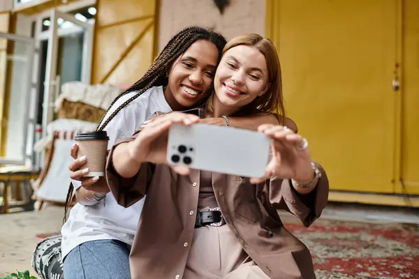 A joyful multiethnic couple shares laughter and coffee while taking a selfie in a cozy cafe setting. — Stock Photo