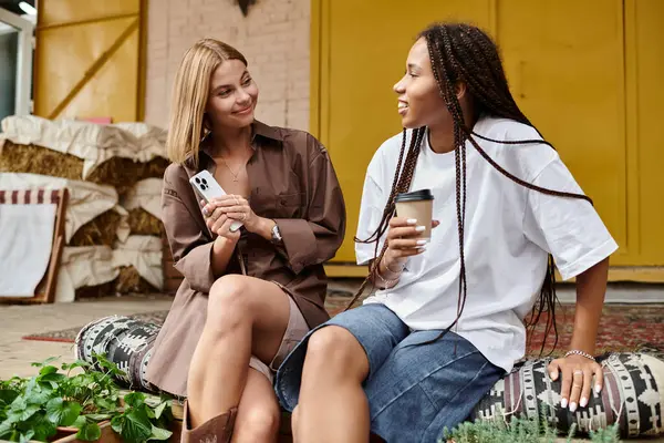 Two women share laughter and love, savoring coffee in a charming cafe filled with greenery. — Stock Photo