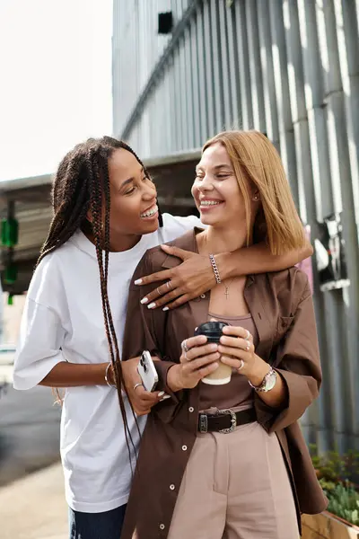 Eine lächelnde Afroamerikanerin mit Zöpfen umarmt ihre Freundin beim Kaffeetrinken. — Stockfoto