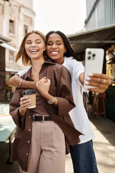 A happy multiethnic couple enjoys a fun moment, smiling and taking a selfie with coffee in hand. — Stock Photo