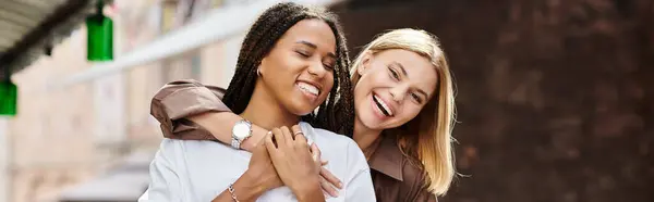 A happy multiethnic lesbian couple embraces, sharing laughter and love on a sunny day. — Stock Photo