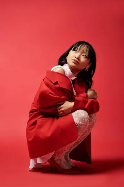 A beautiful Asian woman crouches gracefully in a vibrant red setting. — Stock Photo