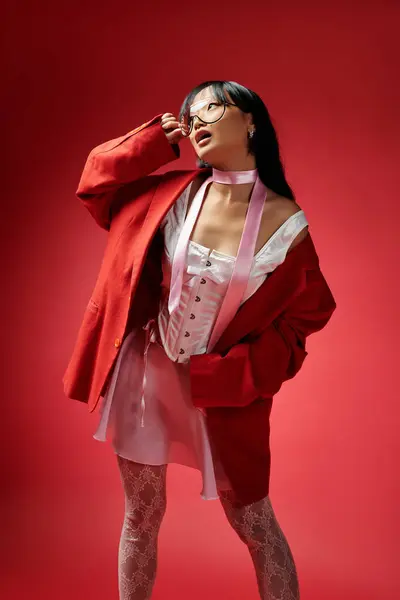 An elegant Asian woman exudes confidence in a fashion forward outfit against a red backdrop. — Stock Photo