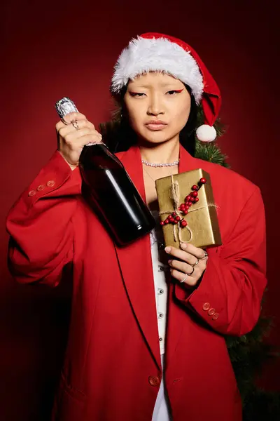 A stylish woman dressed in a vibrant red outfit holds a gift and champagne, exuding festive cheer. — Stock Photo